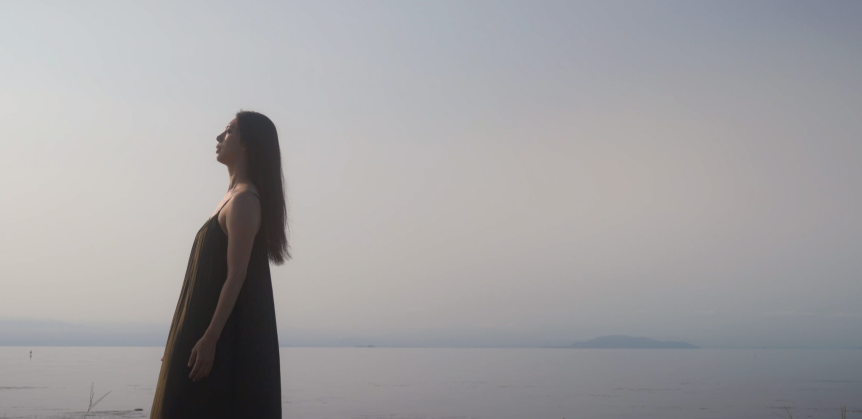 穏やかな海辺で夕日を見つめる女性の姿